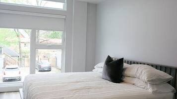 Un dormitorio con un ventanal grande, una cama con ropa blanca y vistas al exterior.