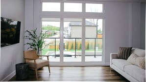 Ein geräumiges Zimmer mit einer großen Schiebeglasdoor, einem bequemen Sofa, einem Korbstuhl und einem kleinen Tisch.