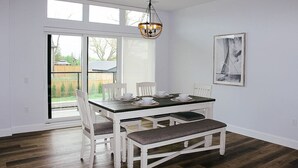 Ein Essbereich mit einem weißen Tisch, Stühlen und einer Bank, einer Chandelier und einer Glastür, die in einen Garten führt.