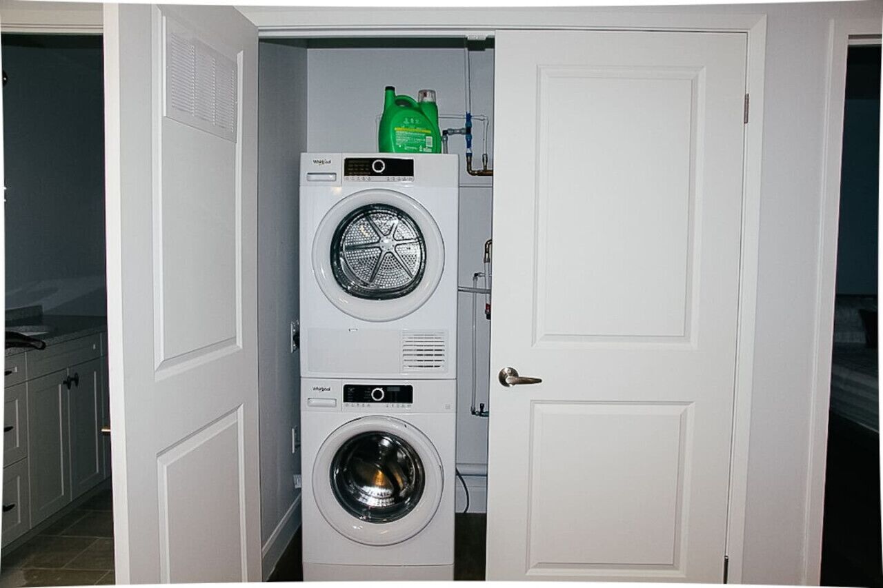 A compact laundry room with two stacked front-loading washing machines and a green detergent bottle on top.