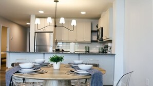 Une cuisine moderne dotée d’un îlot central, d’appareils électroménagers en acier inoxydable et d’un luminaire suspendu.