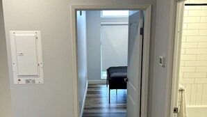 Un pasillo con piso de madera que conduce a un dormitorio con cama y ventana.