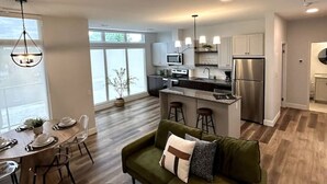 Una cocina moderna con electrodomésticos de acero inoxidable, un comedor con mesa y sillas de madera, y un sofá verde con vista a la cocina.