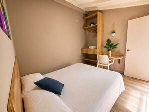 A bedroom with a bed, a desk, a chair, and a door. - Manila by Roots Rentals (Medellín)
