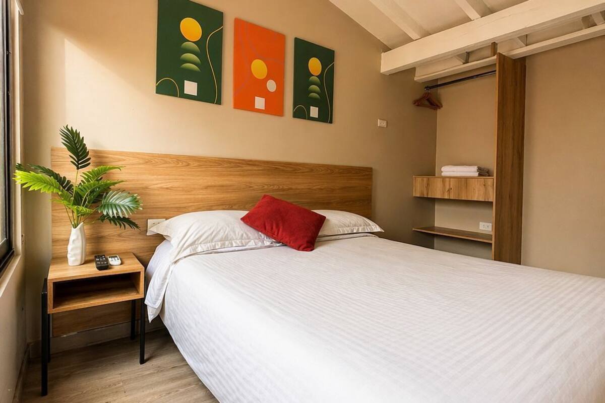 A bedroom with a bed, a nightstand, a plant, and artwork on the wall.