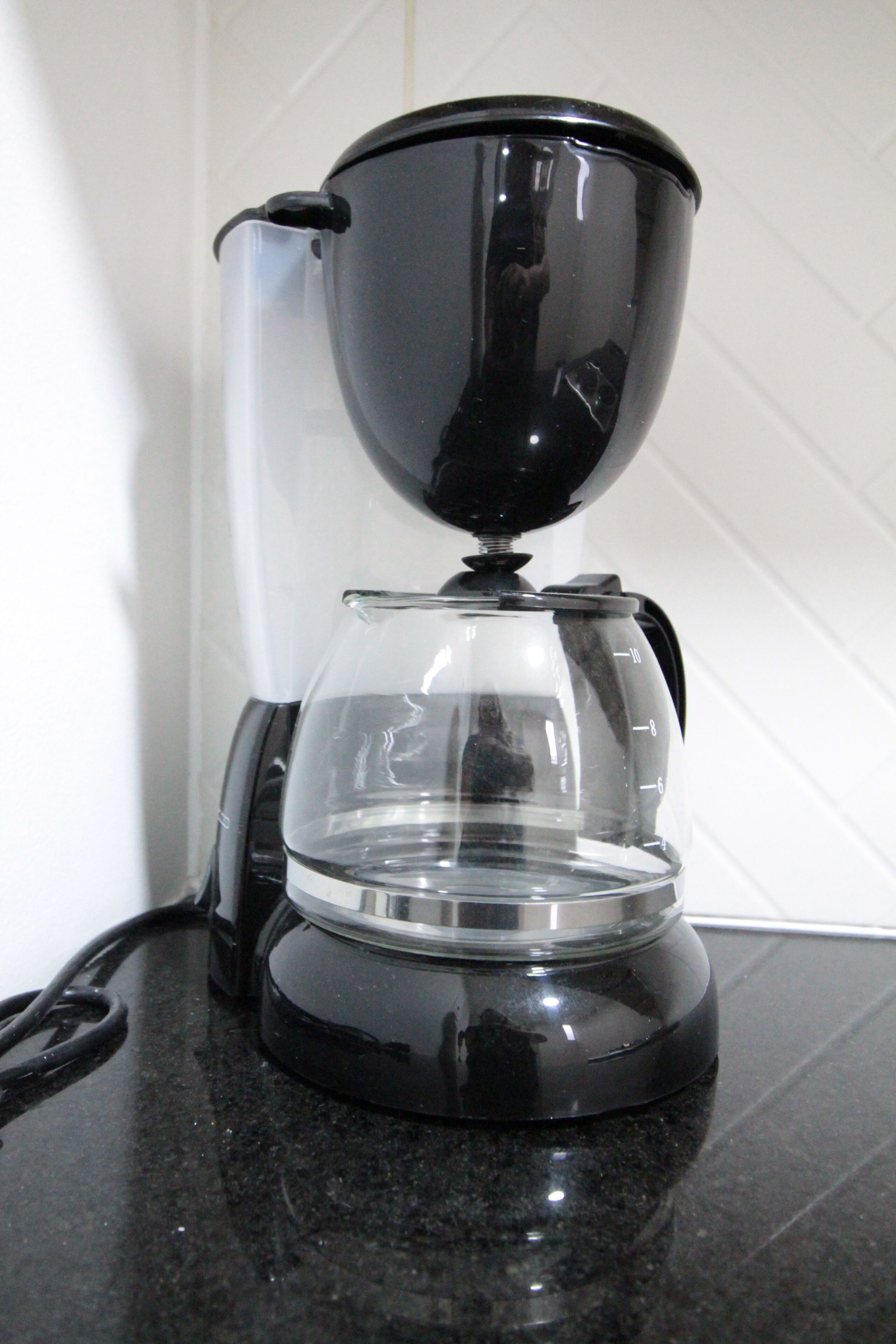 A black coffee maker with a clear glass carafe on a black countertop.