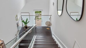 Een moderne trap met donkere houten treden en glazen leuningen, leidend naar een deur met uitzicht op een balkon.