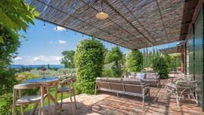 Une terrasse extérieure avec un sol en briques, des meubles en bois et une pergola décorée de guirlandes lumineuses.