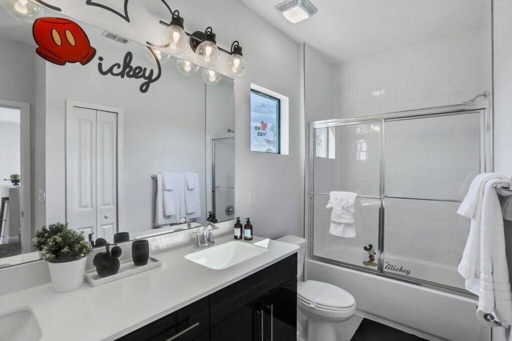 Un baño moderno con un lavamanos blanco, muebles negros, un adorno de Mickey Mouse y un perchero con motivos de Mickey Mouse.