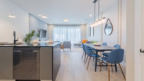 A modern kitchen with a central island, a dining area with blue chairs, and a living space with a sofa and a TV. - TR17145BD - 3 bedrooms home close to Disney (Clermont)