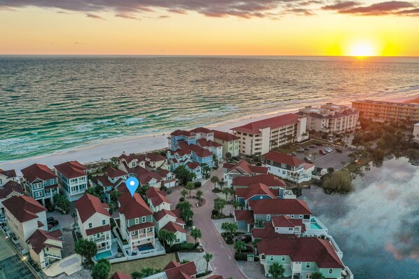 Een woongebied aan de kust met huizen en een hotel, met uitzicht op de oceaan en een zonsondergang.
