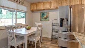 A kitchen with white cabinetry, a stainless steel refrigerator, a dining table with chairs, and a window with blinds.
