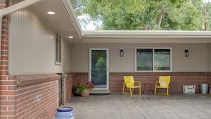 A covered patio with two yellow chairs, a potted plant, and a trash can.