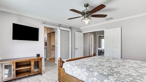 Une chambre à coucher avec un lit, une armoire en bois, un ventilateur de plafond et un téléviseur fixé au mur.