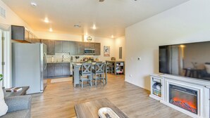 Una sala de estar moderna con chimenea, televisor y cocina al fondo.