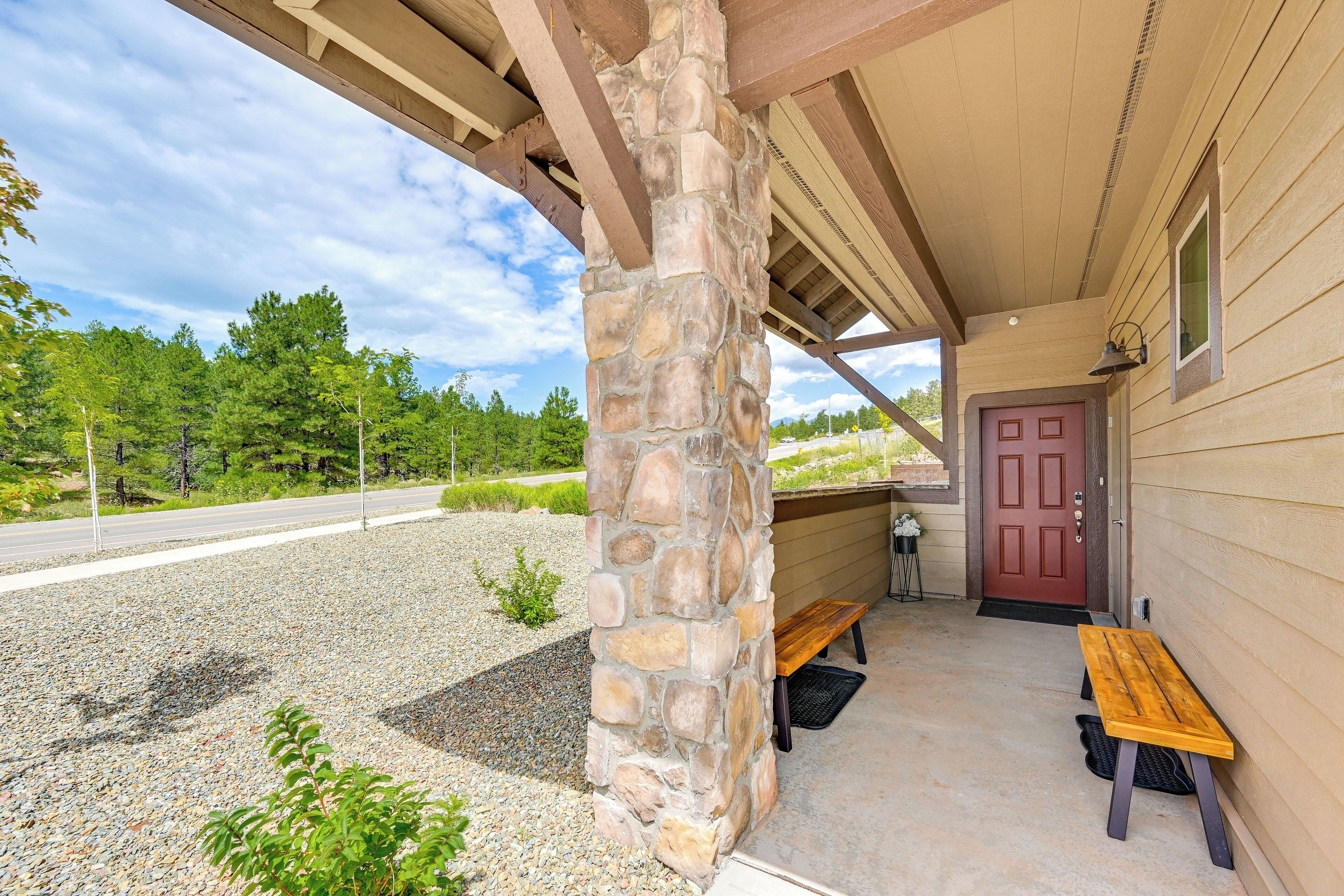 A covered porch with a stone pillar, a wooden bench, and a red door.