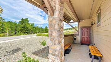 A covered porch with a stone pillar, a wooden bench, and a red door.