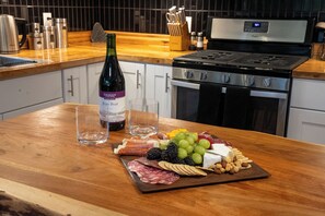 Una encimera de madera con una tabla de embutidos, una botella de vino y copas.