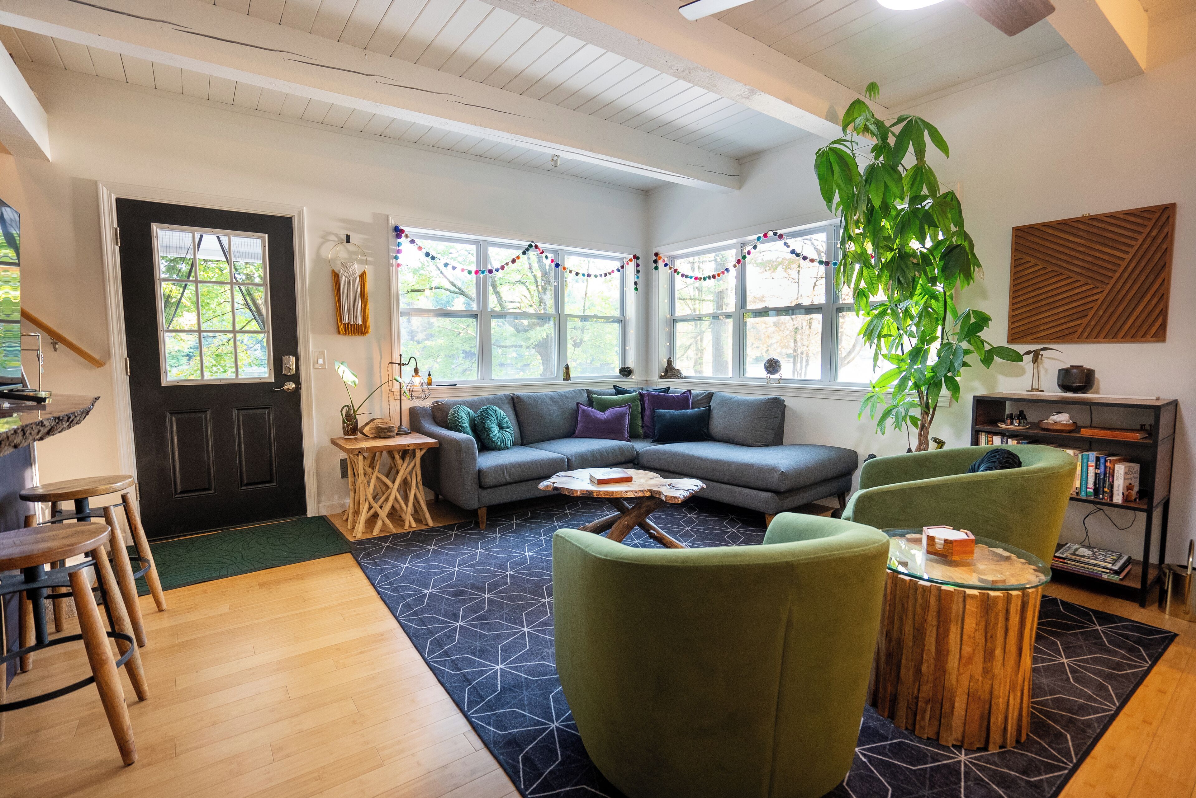 Een gezellige woonkamer met een hoekbank, groene fauteuils, een salontafel en een grote plant.