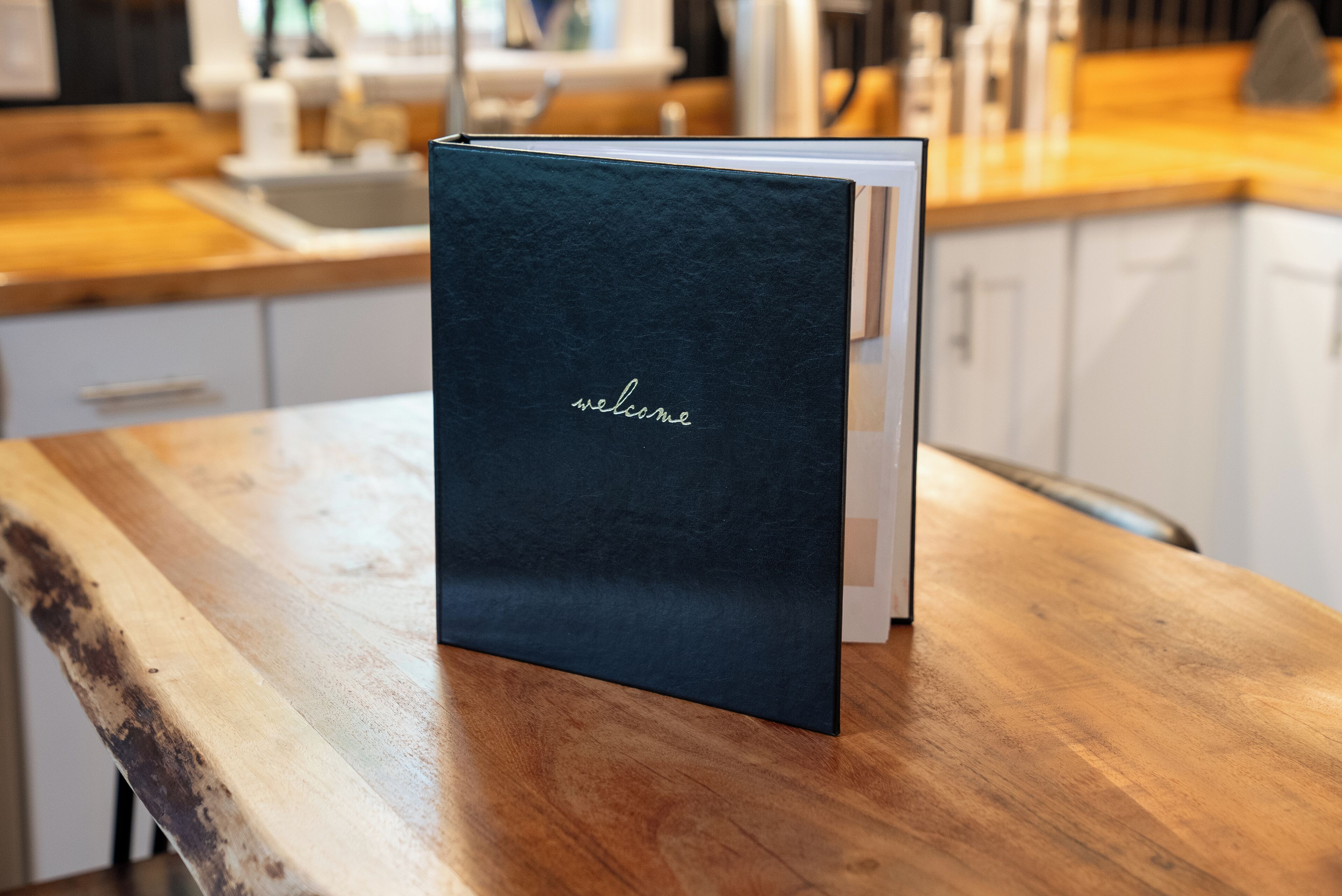 Een donkerblauwe boek met de tekst 'welcome' op een houten tafel.