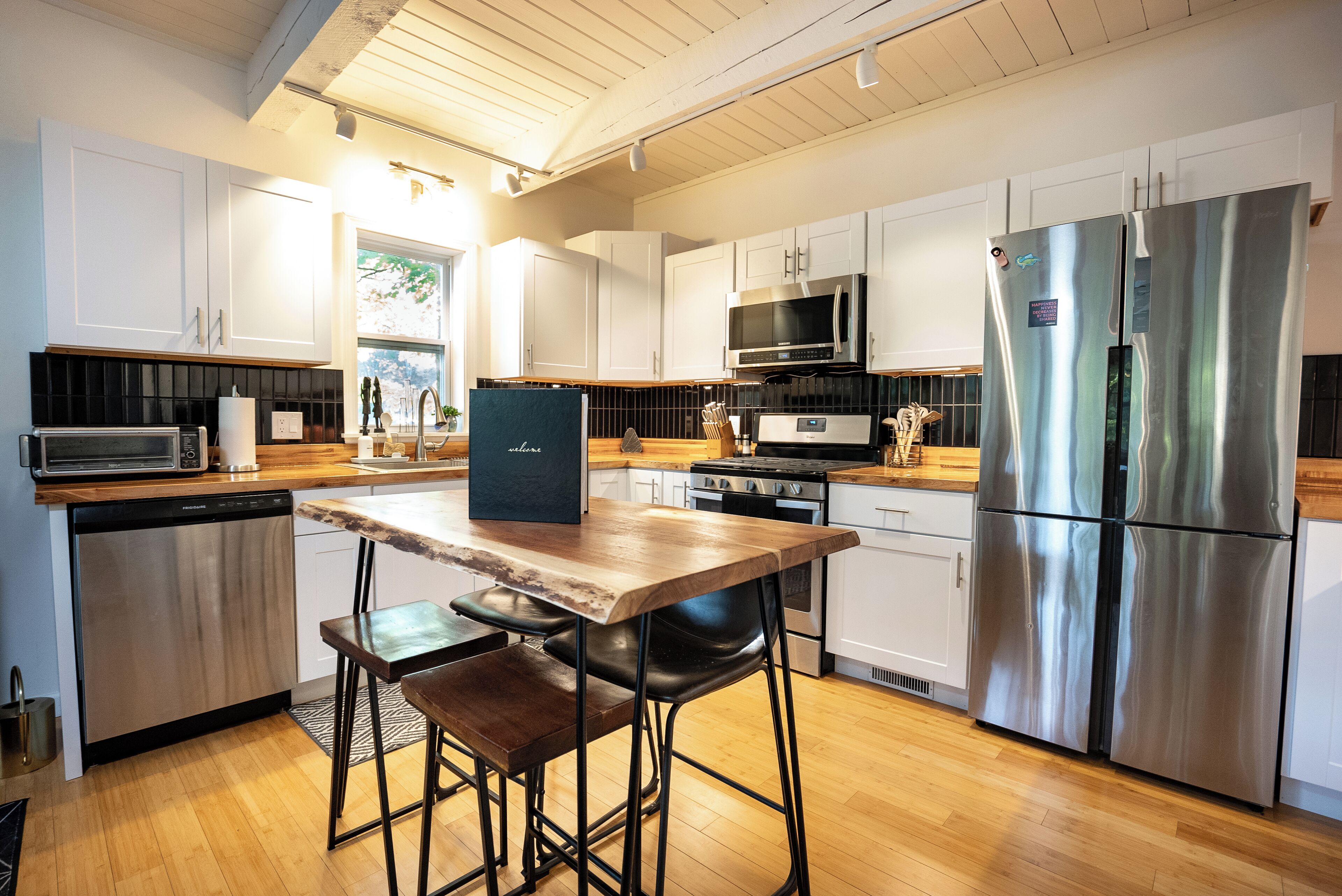 Een moderne keuken met witte kastjes, roestvrijstalen apparatuur, een houten eettafel en barstoelen.