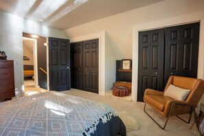 Un dormitorio con una cama, una silla, un aparador y dos puertas.