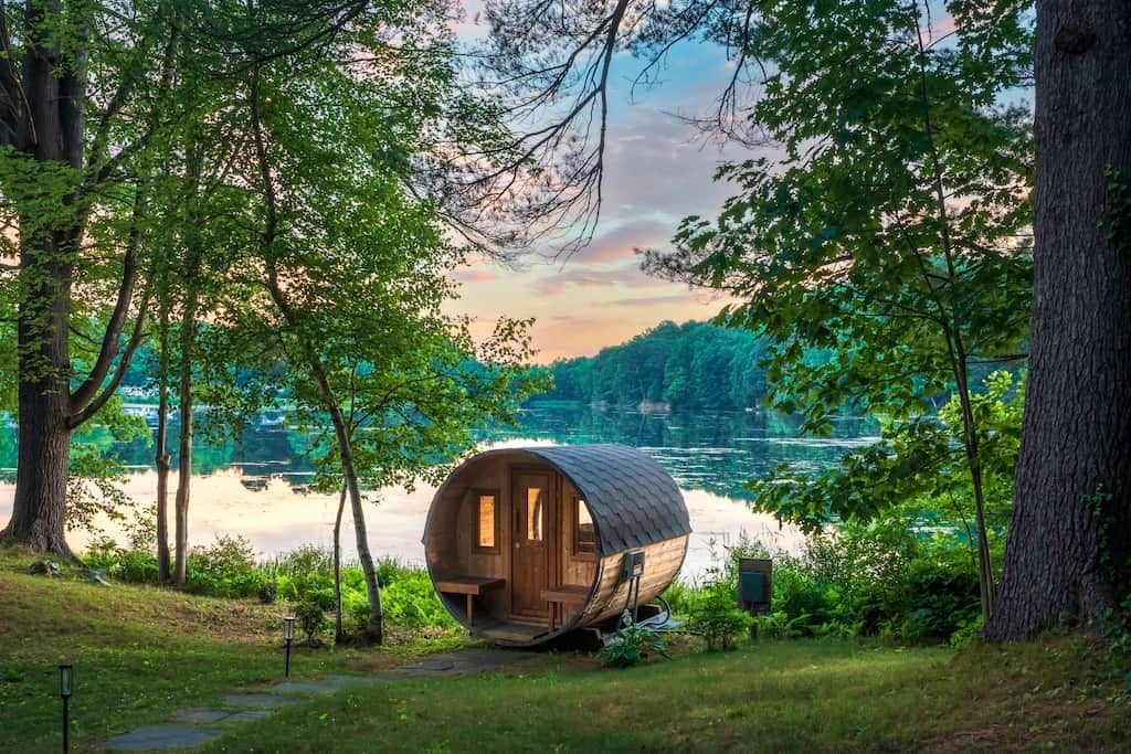 Une cabane en bois avec une porte et des fenêtres, située au bord d’un lac entouré d’arbres.