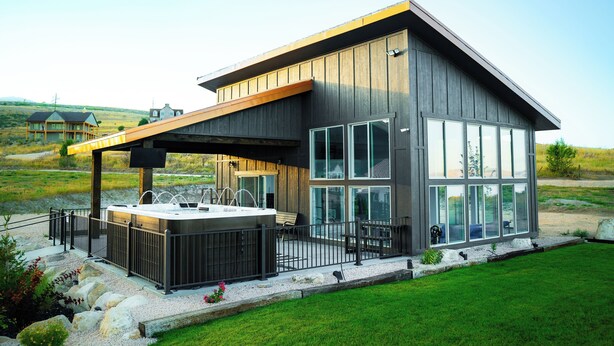 A modern house with a large deck, a hot tub, and a large windowed porch.