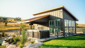 A modern house with a large deck, a hot tub, and a view of the surrounding landscape.