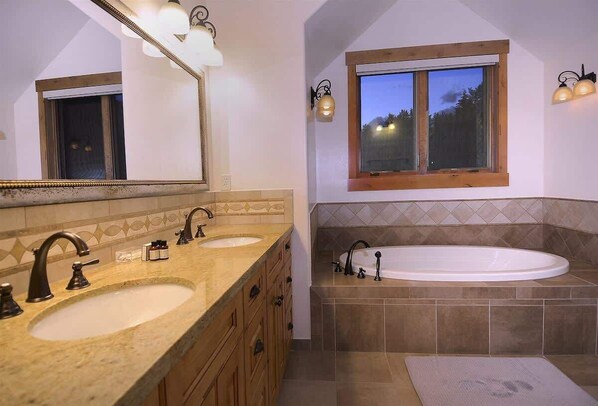 A bathroom with a double sink, a large bathtub, and a window with a view of trees. - Meridian Peaks (Crested Butte)