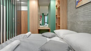 A modern bedroom with a bed, pillows, a wooden wardrobe, and a green accent wall. - Garden Gates by Grand Apartments (Gdansk)
