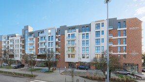 A modern multi-story residential building with a mix of brick and glass facades, balconies, and a gated entrance. - Garden Gates by Grand Apartments (Gdansk)
