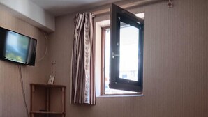 A bedroom with a bed, a TV mounted on the wall, a window with curtains, and a small shelf with a book. - Cosy apartment with balcony (Le Monêtier-les-Bains)