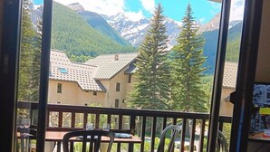 A balcony with a table and chairs, offering a view of mountains and houses. - Cosy apartment with balcony (Le Monêtier-les-Bains)
