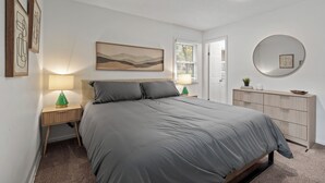 A bedroom with a bed, bedside lamps, a dresser, a mirror, and artwork on the walls. - Spacious 4-bedroom Home in South Kansas City (Kansas City)
