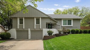 A two-story house with a front garage, a well-maintained lawn, and a brick retaining wall. - Spacious 4-bedroom Home in South Kansas City (Kansas City)