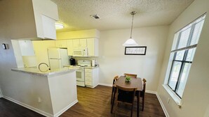 A compact kitchen with white cabinets, a microwave, and a stove. There's a dining table with chairs and a hanging light fixture.