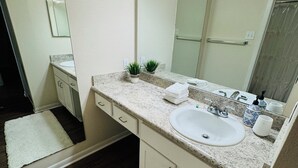 A bathroom with a white sink, a mirror, and a vanity with a countertop. There are two small potted plants on the countertop.