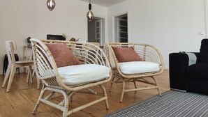 Un salón amplio con sillas de mimbre, un sofá negro y una alfombra estampada.