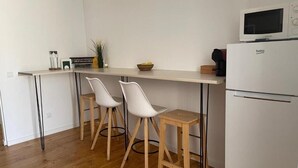 Una cocina compacta con cubierta blanca, dos taburetes blancos tipo barra, un refrigerador blanco y un microondas.