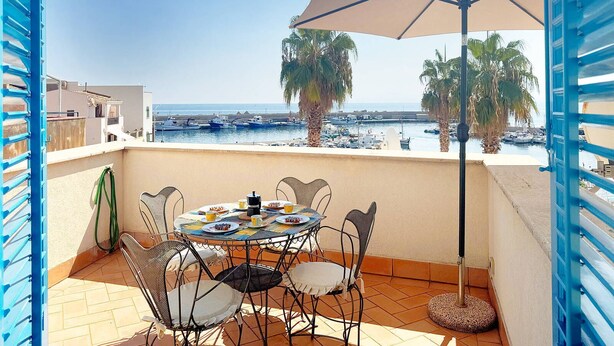 Un balcone con tavolo apparecchiato per mangiare, con vista su una marina piena di barche e palme.