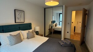 Hotellihuone, jossa on suuri sänky, pääty, yöpöytä lampun kanssa, peili ja ovi, joka johtaa toiseen huoneeseen.