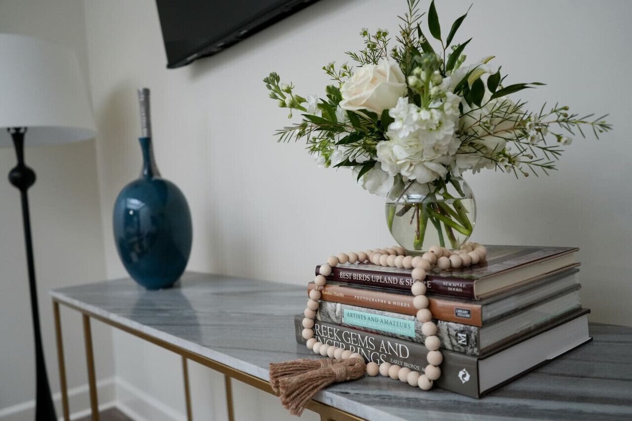 A marble table with a vase of white flowers, a stack of books, and a blue vase.