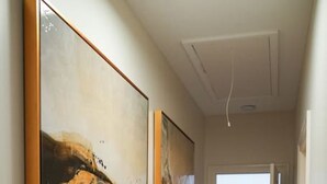 A hallway with two large abstract paintings on the walls, leading to a room with a table and chairs. - The Nook (Demopolis)