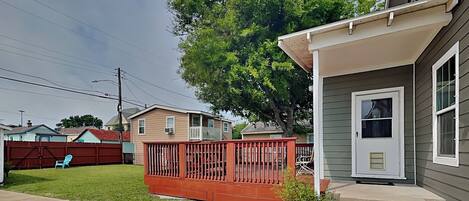 A residential house with a front porch, a red fence, and a small tree.