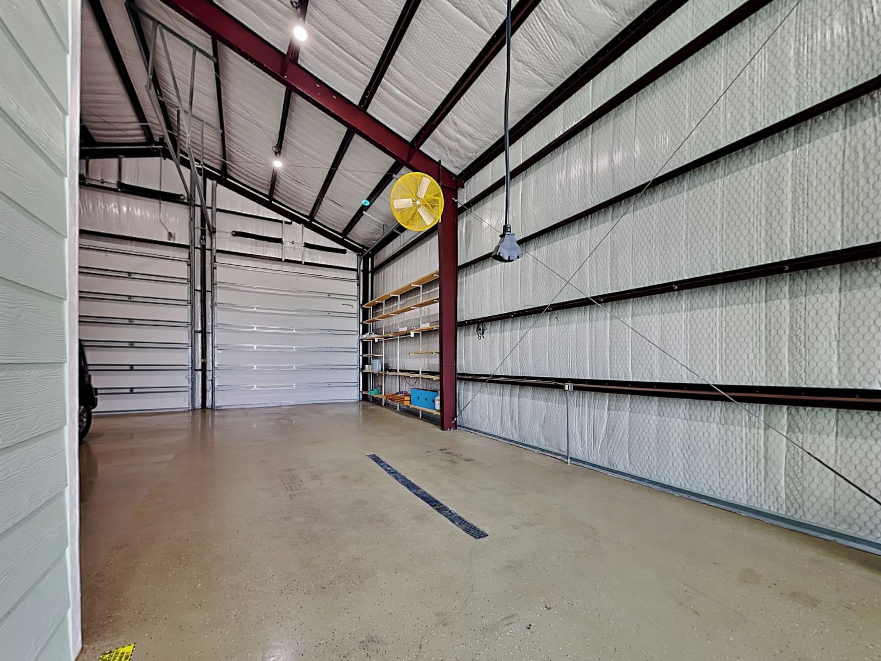 A warehouse interior with metal shelving, a closed garage door, and a yellow fan.