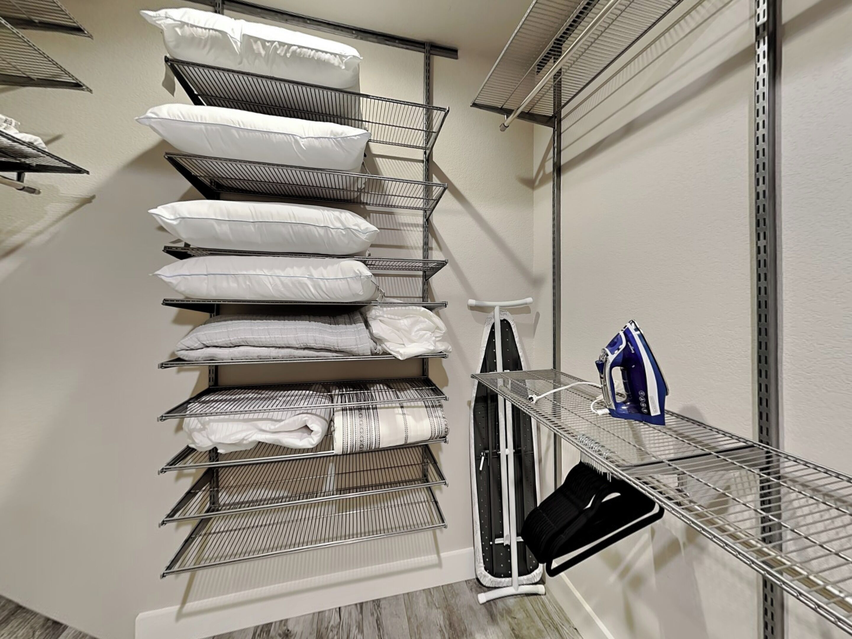 A storage closet with shelves holding pillows, folded blankets, and a vacuum cleaner.