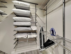 A storage closet with shelves holding pillows, folded blankets, and a vacuum cleaner. - Heron's Roost by Miss Kitty’s (Rockport)