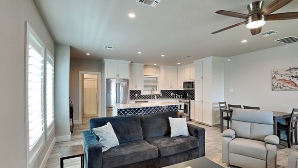 A modern living room with a dark grey sofa, a light grey armchair, and a wooden coffee table. A ceiling fan and recessed lighting are visible. - Heron's Roost by Miss Kitty’s (Rockport)