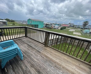 A wooden deck with a railing, a turquoise chair, and a view of a residential area with houses and a body of water in the background.